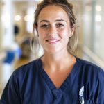 late-20s New Zealand travelling nurse working in London, standing in a quiet London hospital ward hallway